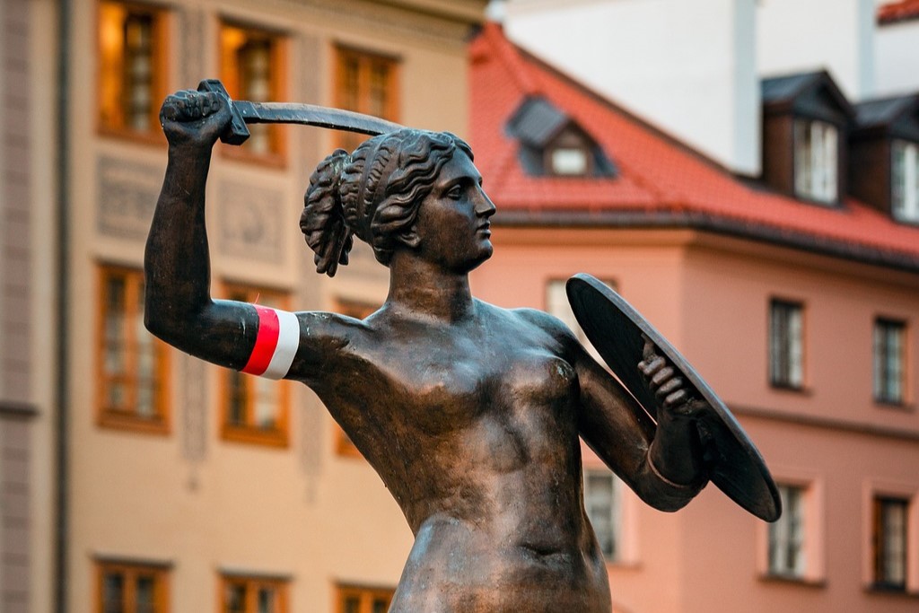 Zdjęcie przedstawiające górną cześć postaci pomnika syrenki warszawskiej z biało-czerwoną opaską na ramieniu