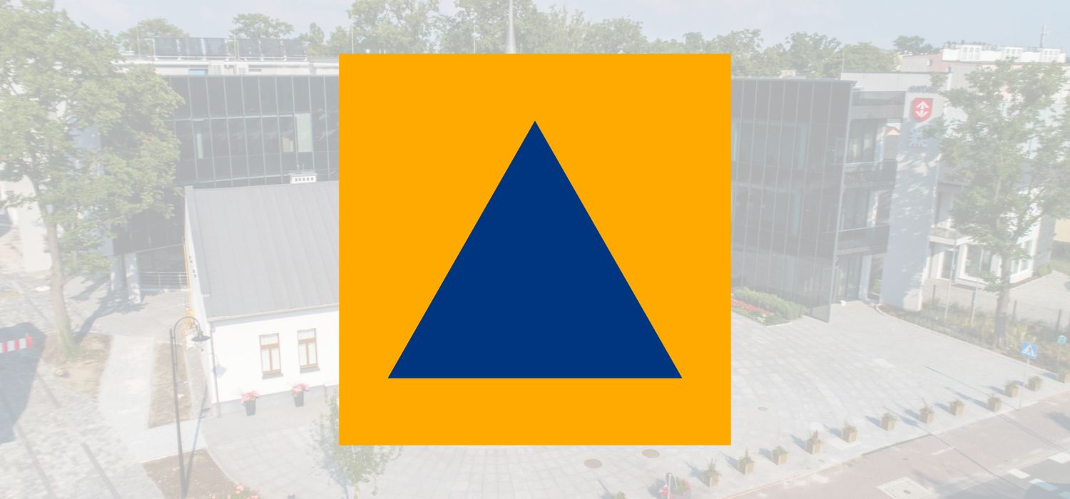 Granatowy trójkąt równoboczny w żółtym kwadracie - logotyp Obrony Cywilnej, w tle zdjęcie Urzędu Miejskiego i Willi Niespodzianka